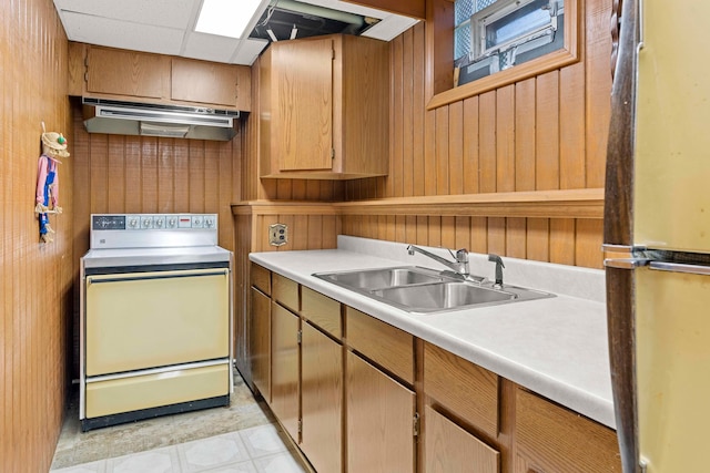 kitchen with sink, stainless steel refrigerator, light tile patterned flooring, wood walls, and electric range