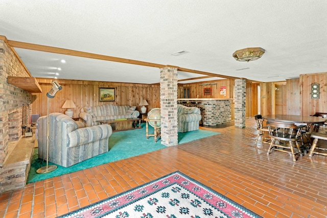 living room with brick wall, wood walls, a textured ceiling, and ornate columns