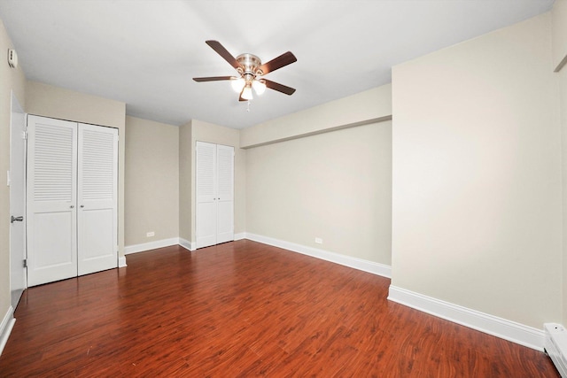 unfurnished bedroom featuring multiple closets, dark hardwood / wood-style floors, and ceiling fan