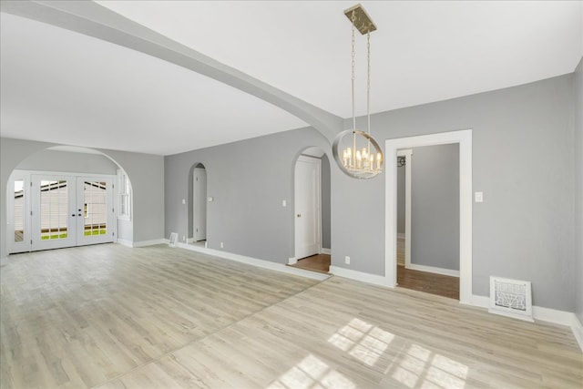 unfurnished dining area with a notable chandelier, light hardwood / wood-style flooring, and french doors