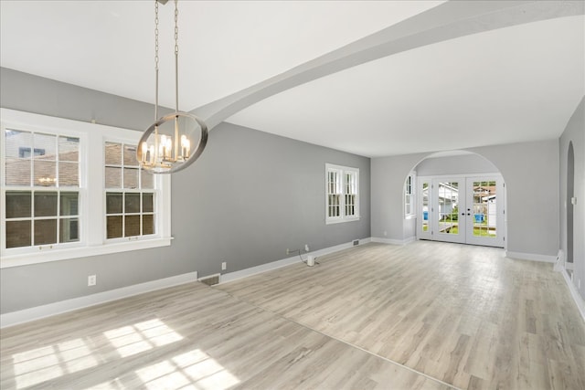 unfurnished living room featuring a notable chandelier, french doors, and light wood-type flooring