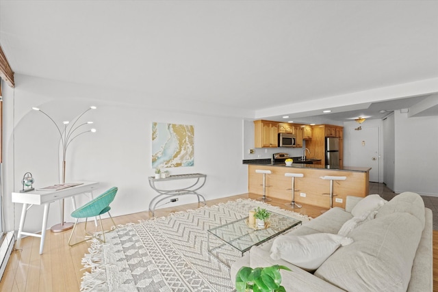 living room featuring baseboard heating, sink, and light hardwood / wood-style floors