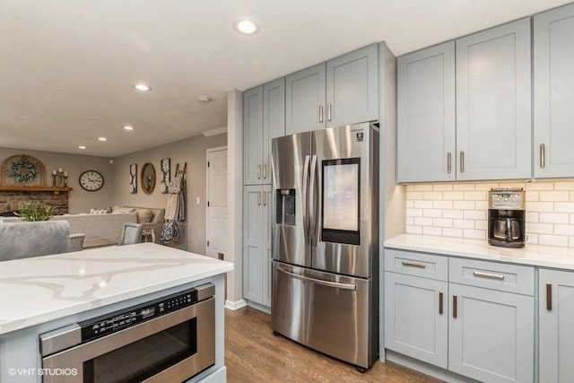 kitchen featuring gray cabinetry, light wood-type flooring, stainless steel appliances, light stone countertops, and decorative backsplash