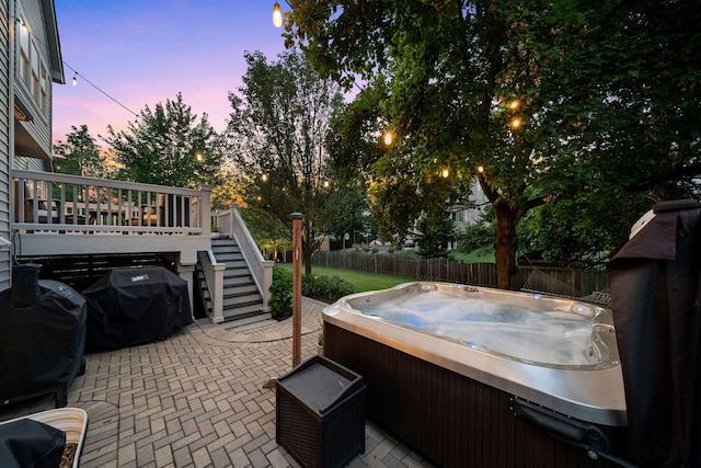 patio terrace at dusk with area for grilling, a deck, and a hot tub