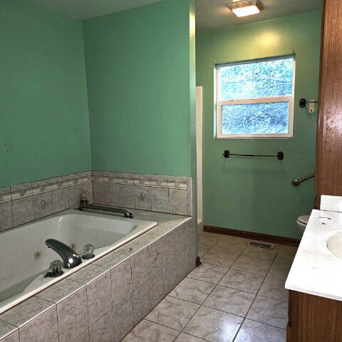 bathroom with vanity, tiled bath, and toilet