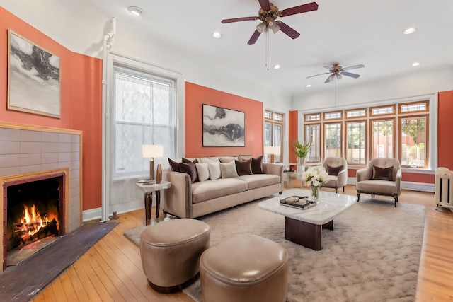 living room featuring ceiling fan, a tile fireplace, and light hardwood / wood-style floors