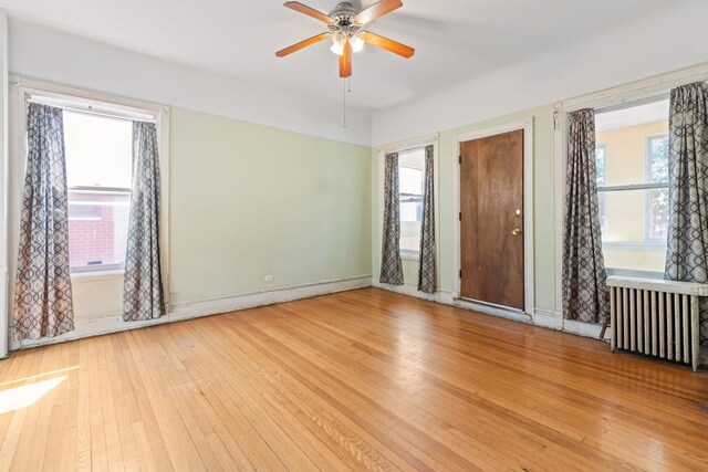 unfurnished room featuring radiator heating unit, a healthy amount of sunlight, ceiling fan, and light hardwood / wood-style floors