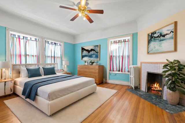 bedroom featuring radiator heating unit, light wood-type flooring, multiple windows, and a tile fireplace