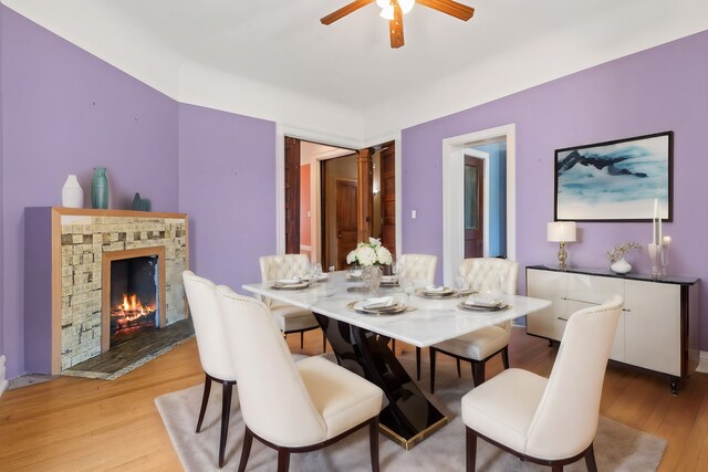 dining area featuring ceiling fan, a stone fireplace, and light hardwood / wood-style floors