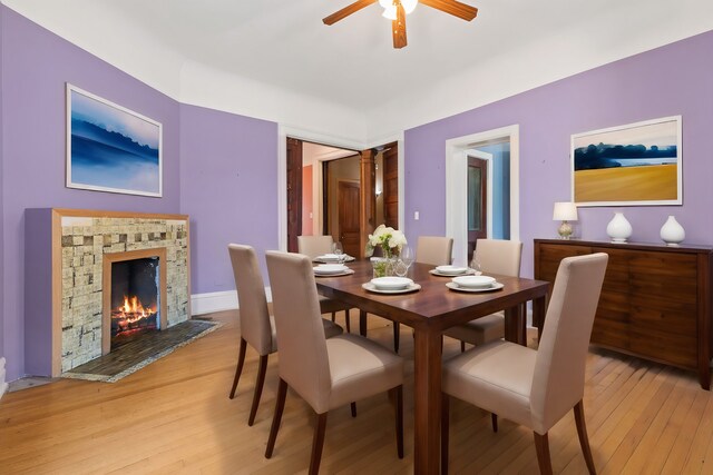 dining space featuring ceiling fan, light hardwood / wood-style flooring, and a stone fireplace