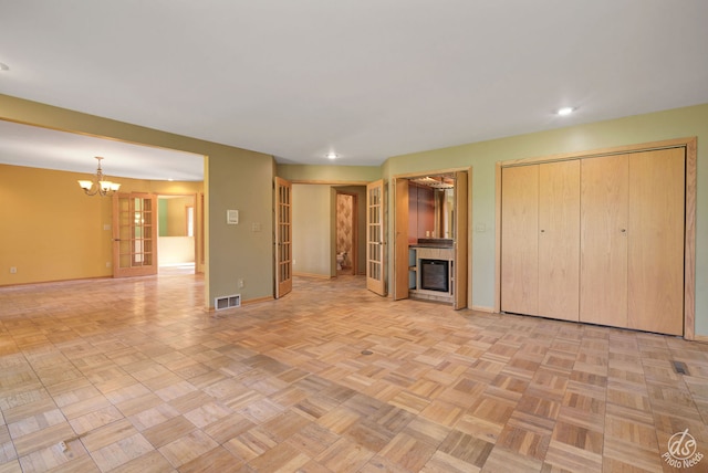 unfurnished living room with light parquet floors, an inviting chandelier, and french doors