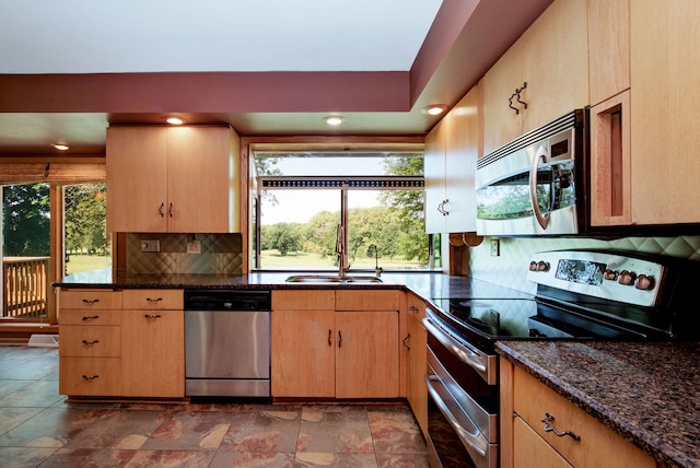 kitchen with appliances with stainless steel finishes, backsplash, light brown cabinetry, sink, and dark stone countertops