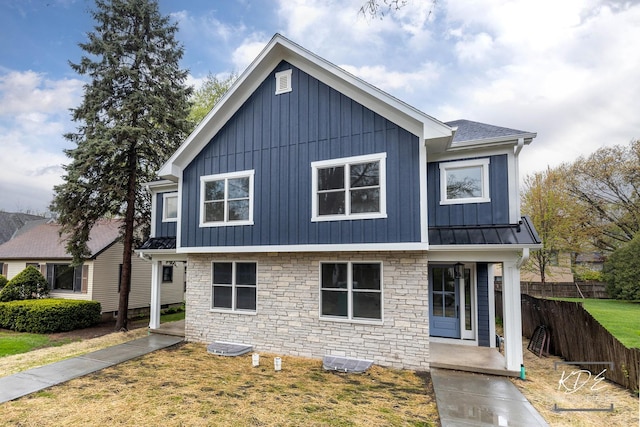 view of front of home with a standing seam roof, fence, and stone siding