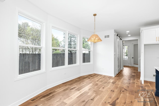 unfurnished dining area featuring a barn door, baseboards, light wood-style flooring, and visible vents