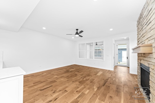 unfurnished living room featuring a stone fireplace, light wood-style flooring, a ceiling fan, baseboards, and recessed lighting