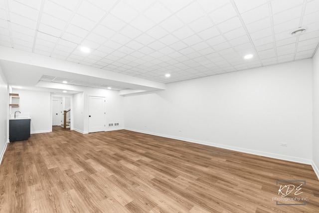 finished basement featuring visible vents, baseboards, light wood-type flooring, recessed lighting, and a sink
