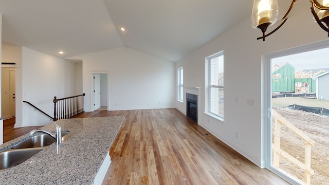 kitchen featuring light stone countertops, sink, light wood-type flooring, and vaulted ceiling