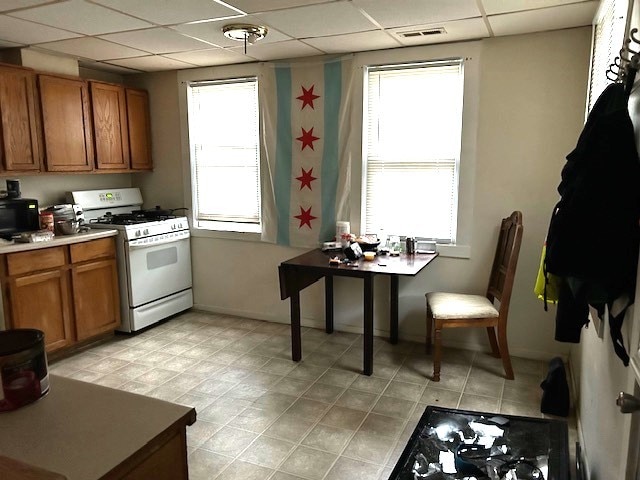 kitchen with a drop ceiling, white range with gas stovetop, and light tile patterned floors