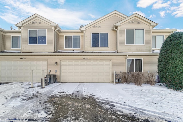 snow covered property with cooling unit and a garage