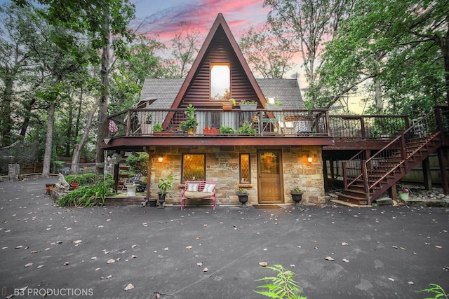 view of front of house featuring stone siding, a patio, stairway, and a wooden deck