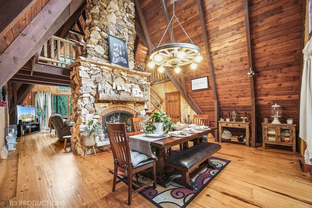 dining space with light wood-type flooring, high vaulted ceiling, wood walls, wooden ceiling, and a fireplace