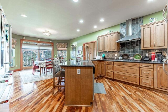 kitchen featuring light wood-type flooring, a kitchen breakfast bar, sink, tasteful backsplash, and wall chimney exhaust hood