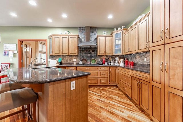 kitchen with light hardwood / wood-style flooring, wall chimney range hood, a kitchen breakfast bar, backsplash, and sink