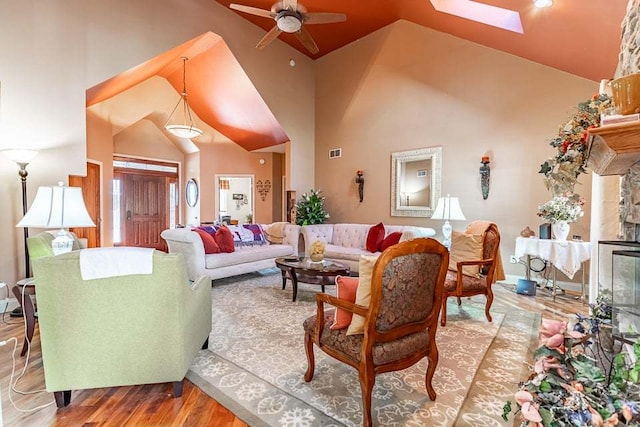 living room with ceiling fan, wood-type flooring, a skylight, and high vaulted ceiling