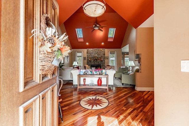 foyer with hardwood / wood-style floors, ceiling fan, a stone fireplace, a skylight, and high vaulted ceiling