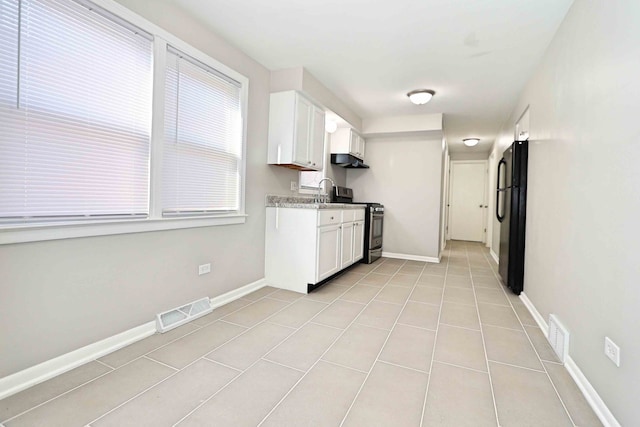 kitchen with white cabinetry, black fridge, light tile patterned floors, and stainless steel stove