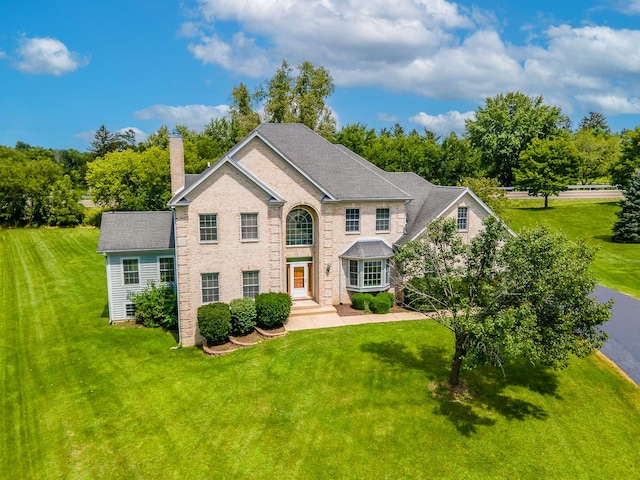 view of front of house featuring a chimney, a front lawn, and brick siding