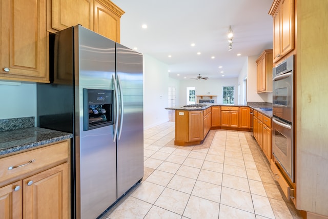 kitchen featuring stainless steel appliances, kitchen peninsula, ceiling fan, dark stone counters, and light tile patterned flooring