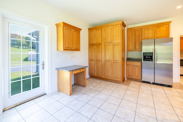 kitchen featuring stainless steel fridge with ice dispenser, dark stone countertops, and light tile patterned floors