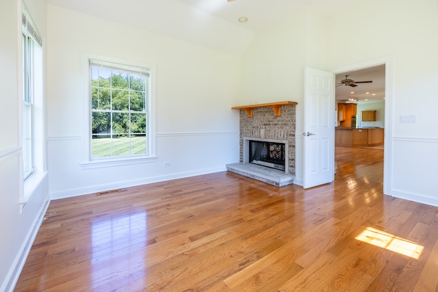 unfurnished living room featuring a fireplace, light wood-type flooring, vaulted ceiling, and ceiling fan