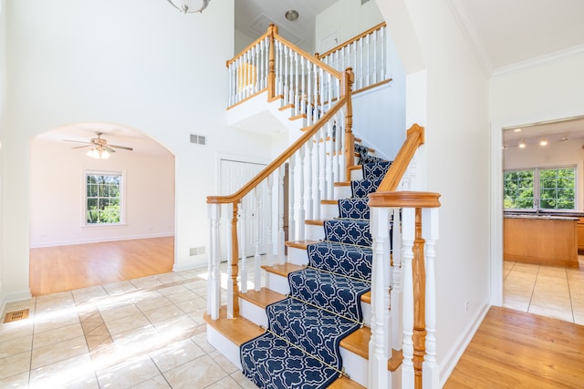 stairs featuring a towering ceiling, wood-type flooring, crown molding, and ceiling fan