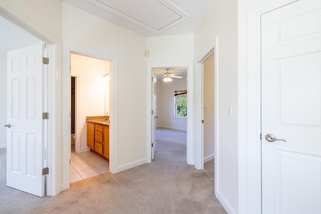 corridor featuring baseboards, light tile patterned floors, attic access, and light colored carpet