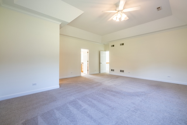 spare room with a tray ceiling, ceiling fan, light carpet, and ornamental molding