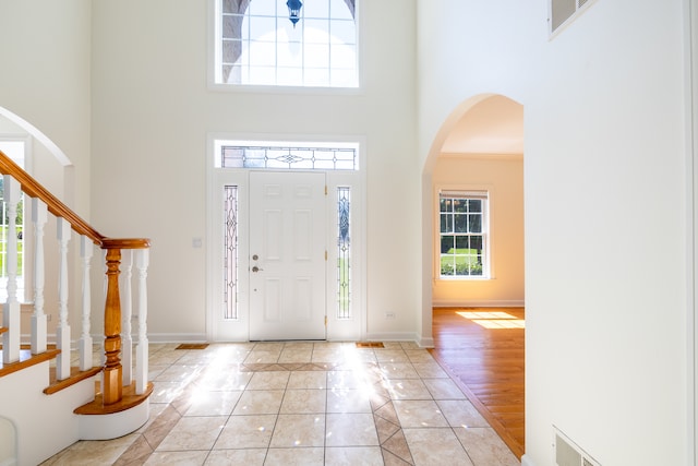 foyer entrance with a wealth of natural light, ornamental molding, a towering ceiling, and light hardwood / wood-style floors