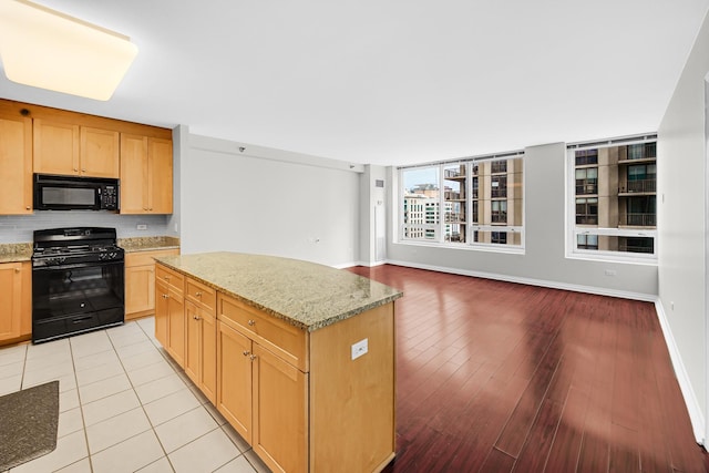 kitchen with light stone countertops, a center island, light hardwood / wood-style floors, and black appliances