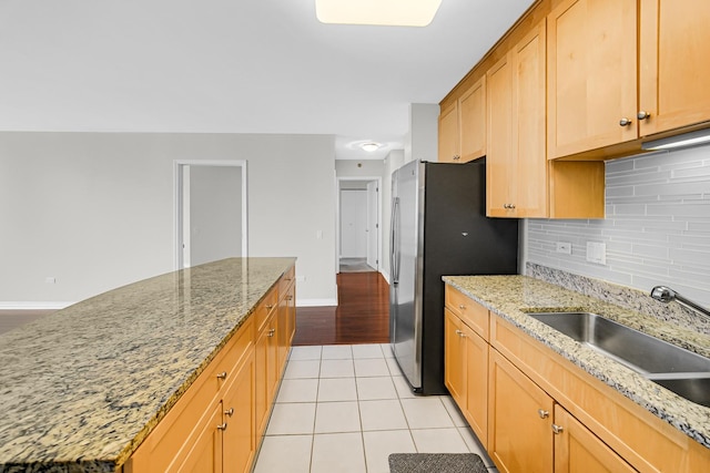 kitchen featuring sink, light tile patterned floors, stainless steel fridge, backsplash, and light stone counters