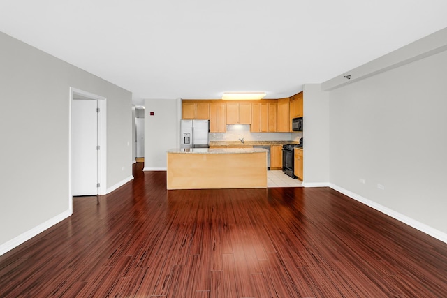 kitchen with hardwood / wood-style flooring, a center island, tasteful backsplash, light stone counters, and black appliances