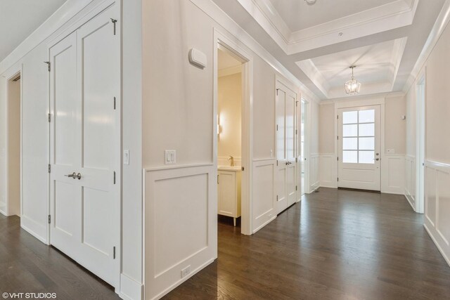 unfurnished living room with ornamental molding, an inviting chandelier, a raised ceiling, and dark wood-type flooring