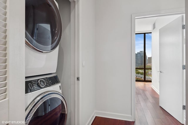 laundry room with stacked washer and dryer, laundry area, baseboards, a view of city, and dark wood finished floors