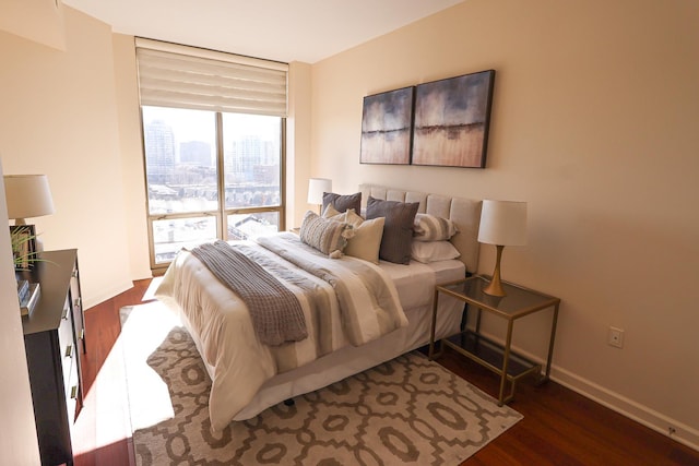 bedroom with baseboards, dark wood-style flooring, and a city view