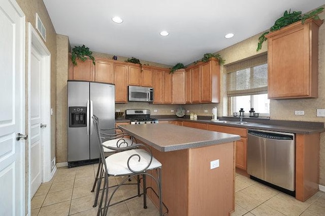 kitchen with a kitchen island, sink, a kitchen bar, light tile patterned floors, and stainless steel appliances