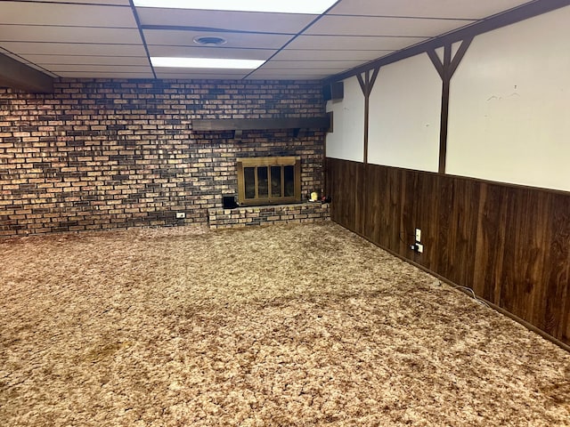 basement with brick wall, a drop ceiling, carpet, and a brick fireplace