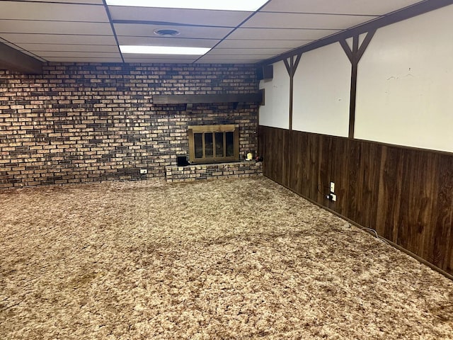 finished basement featuring a drop ceiling, a wainscoted wall, carpet flooring, and wood walls