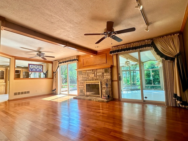 unfurnished living room featuring light hardwood / wood-style flooring, a stone fireplace, a textured ceiling, and ceiling fan