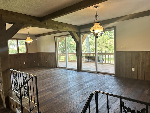 unfurnished living room featuring hardwood / wood-style floors, a textured ceiling, wainscoting, and beam ceiling