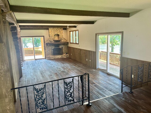 unfurnished living room with a wainscoted wall, a healthy amount of sunlight, beamed ceiling, and wood-type flooring
